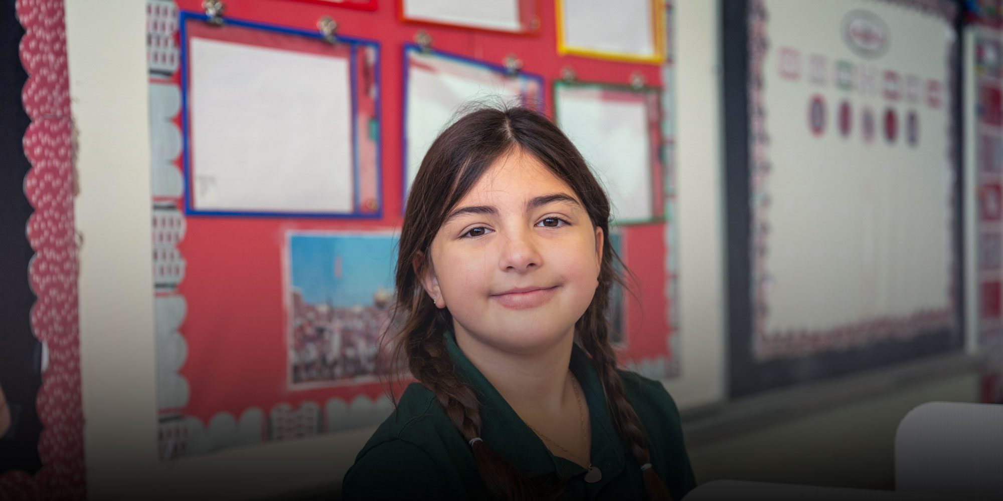 Smiling student with pigtails sitting in a classroom.