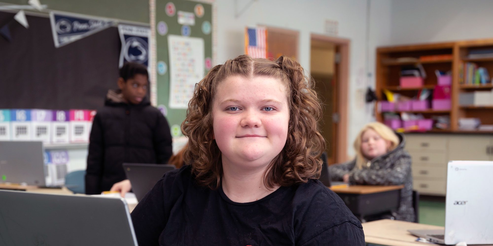 Smiling student sitting at a classroom desk with a laptop.